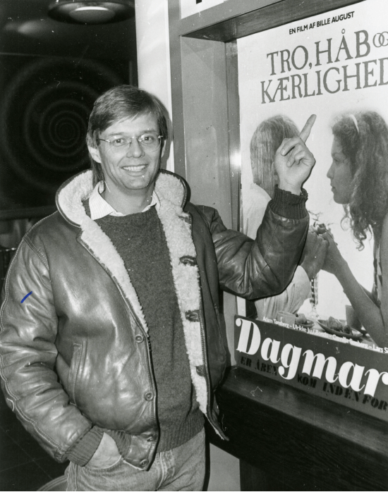 Bille August foran filmplakaten til "Tro, håb og kærlighed" fra 1984, der havde Camilla Søeberg i en af hovedrollerne.