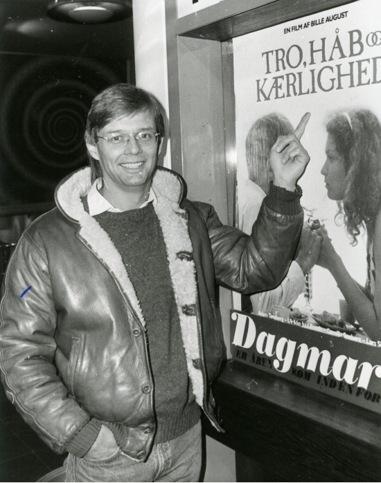 Bille August foran filmplakaten til "Tro, håb og kærlighed" fra 1984, der havde Camilla Søeberg i en af hovedrollerne. 