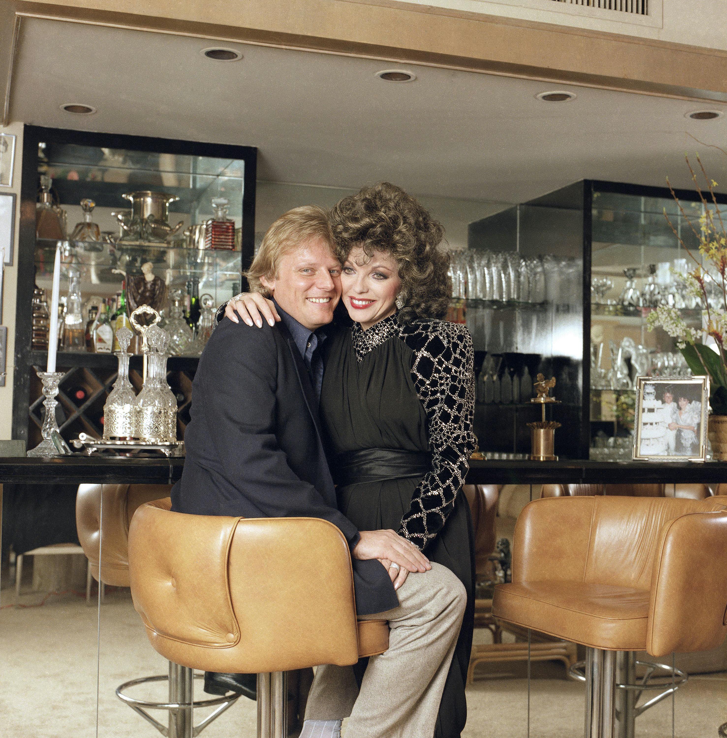 Actress Joan Collins and her husband Peter Holm pose for a photographer in the living room of their home in Beverly Hills, Feb. 1, 1986. (AP Photo/Mark Sennett)