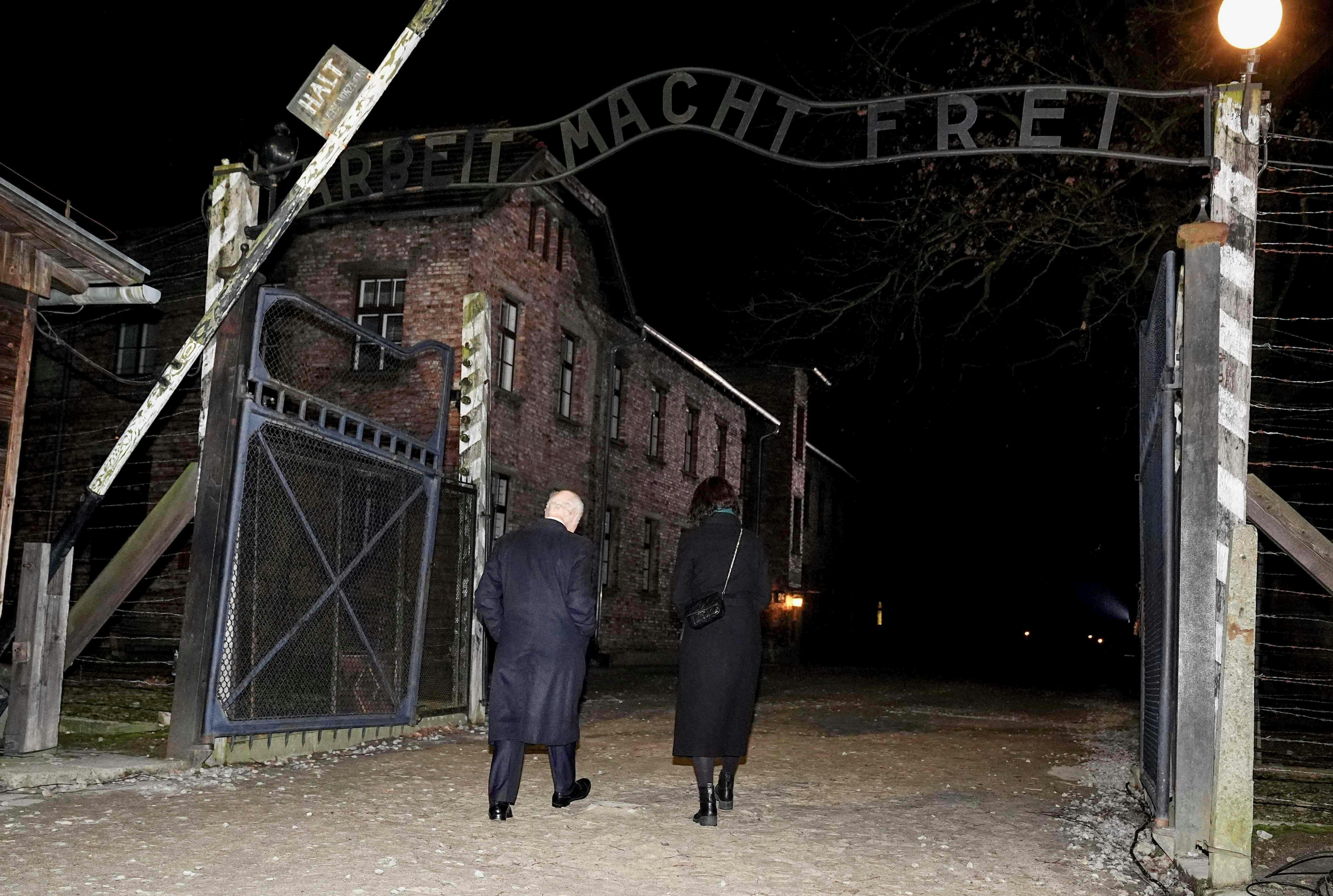 Kong Charles under "Arbeit macht frei"-skiltet.