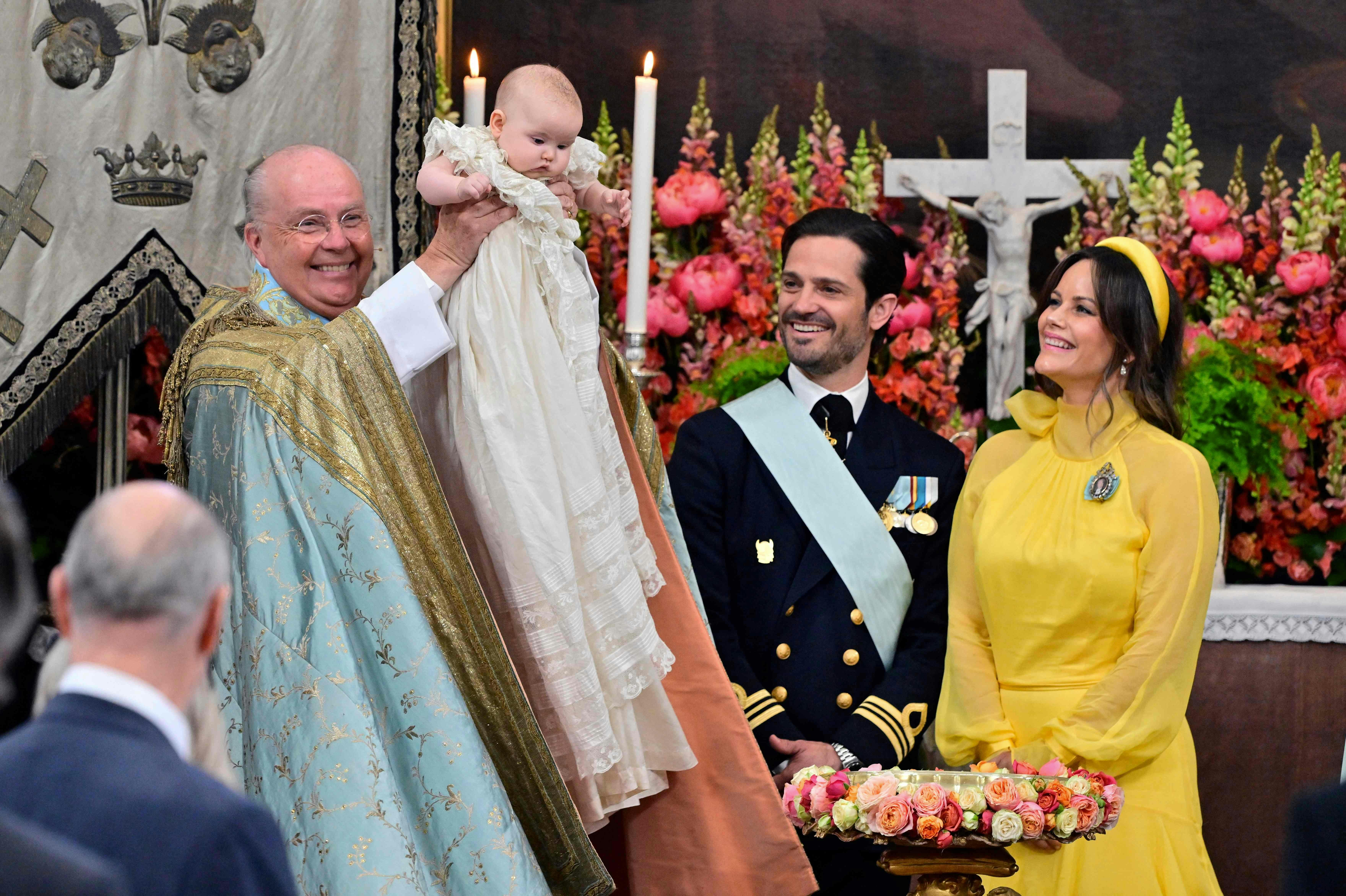 The chief priest, Bishop Johan Dalman (L) holds up Princess Ines of Sweden after he baptized her, as Prince Carl Philip of Sweden (2nd R) and Princess Sofia of Sweden (R) look on, during Princess Ines's baptism in Drottningholm Palace Chapel in Stockholm, Sweden, on June 13, 2025. (Photo by Jonas EKSTROMER / TT News Agency / AFP) / Sweden OUT