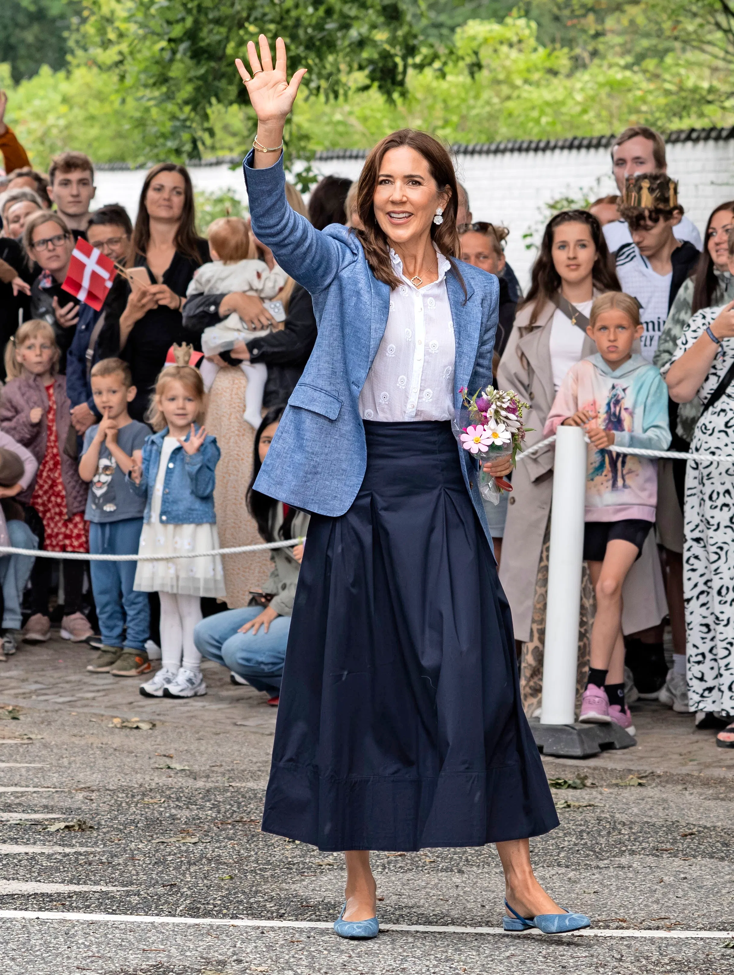 Dronning Mary i sort nederdel med hvid skjorte og blå blazer, der matcher hendes Chanel-sandaler.