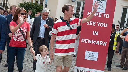 Lille prins Henrik kigger nysgerrigt med, mens mor og far i højt humør hilser på ved den danske udstilling.